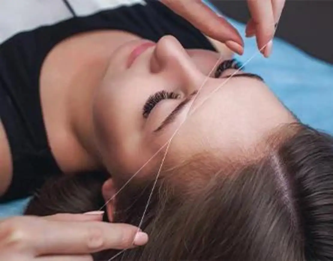 A woman receiving professional eyebrow shaping, showcasing a focused and skilled beautician at work.